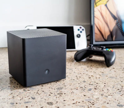 Black cube speaker with a gaming console and controller on a terrazzo countertop.