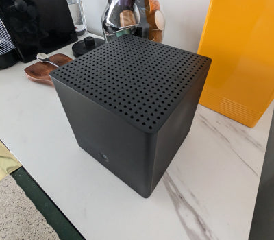 Black perforated cube on a countertop next to a yellow appliance and other items.