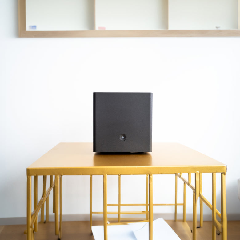 A black speaker sits on a wooden table in a minimalist room.