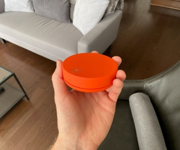 Hand holding an orange circular device in a living room setting.