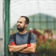 Man standing in a greenhouse with crossed arms, surrounded by plants.