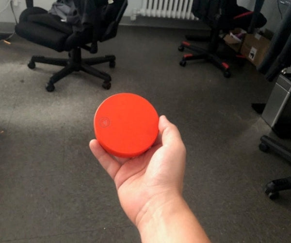 Person holding a round, red device in an office setting.
