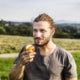 A person eating an apple in a grassy field.