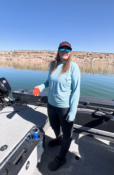 Woman standing on a boat holding an orange object, with a lake in the background.
